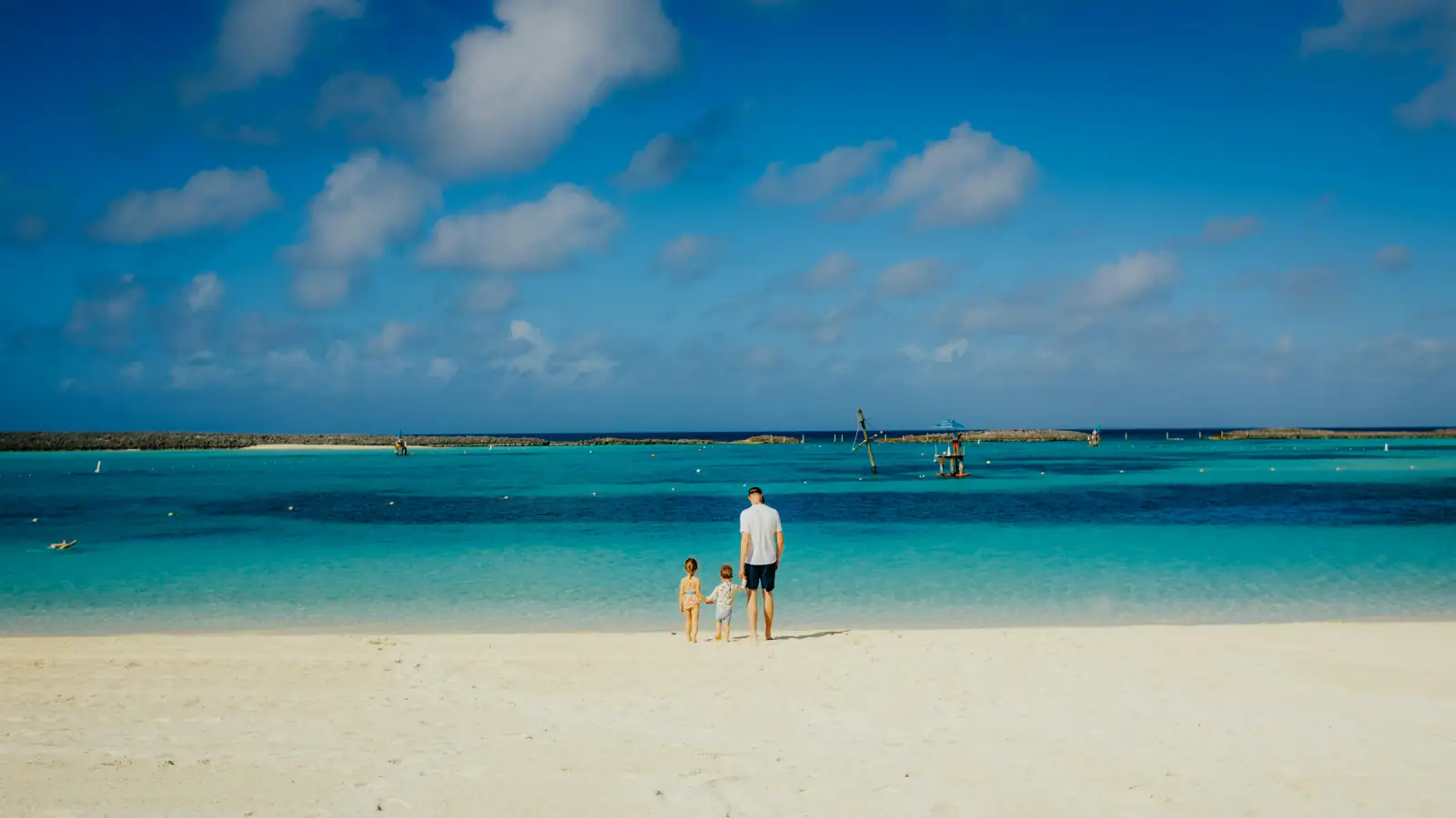 A parent and two children at the edge of a turquoise Caribbean lagoon