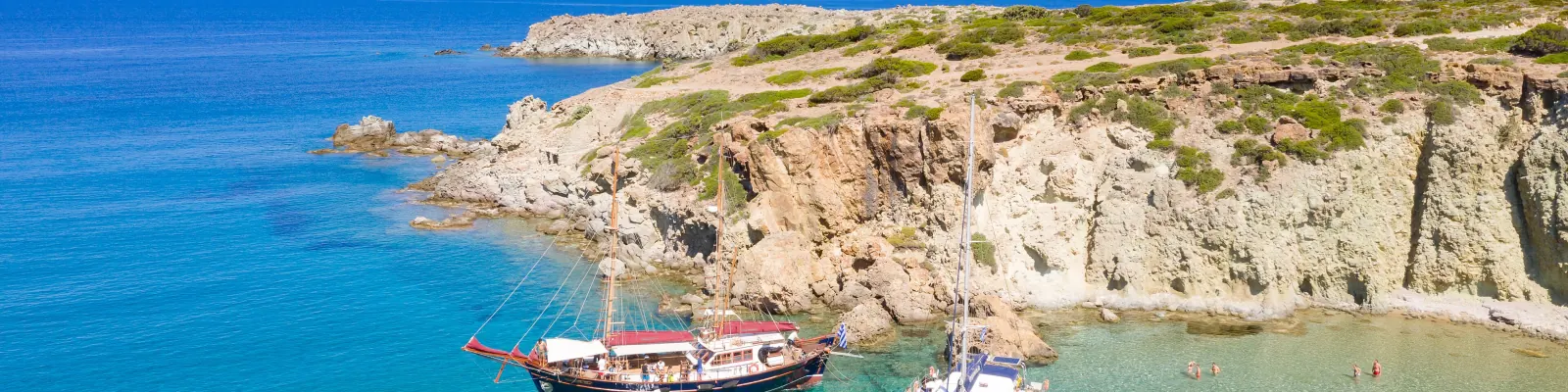 A wooden schooner and a catamaran at anchor in turquoise water below the cliffs of Kleftiko, Milos