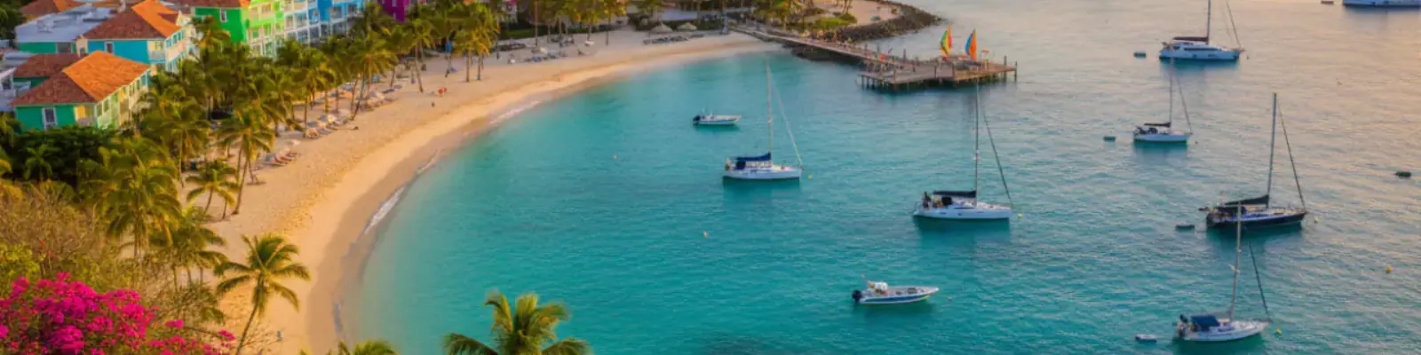 A crescent of white sand and palms around a turquoise bay with yachts at anchor