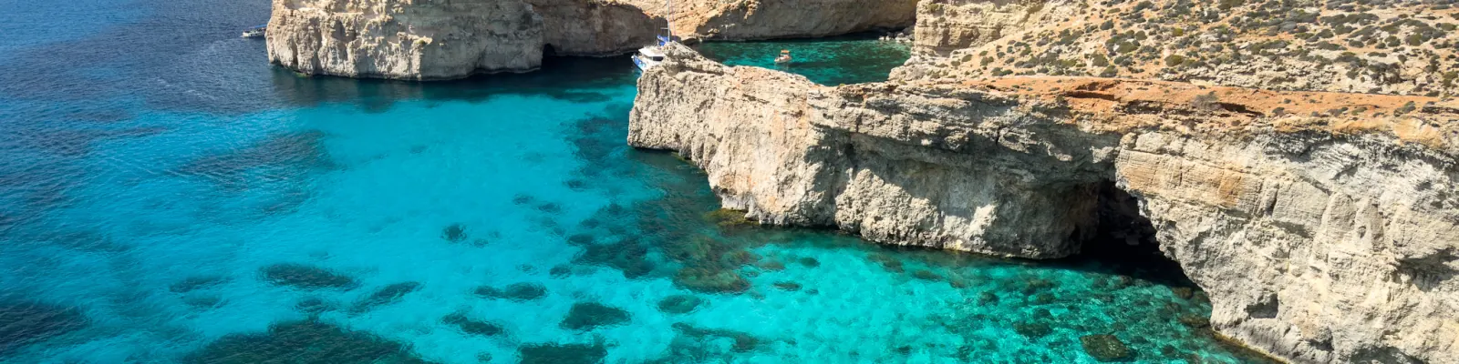 Clear turquoise water between white limestone cliffs and sea arches at the Crystal Lagoon, Comino